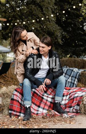 young woman in trench coat looking at cheerful man sitting on blanket in park,stock image Stock Photo
