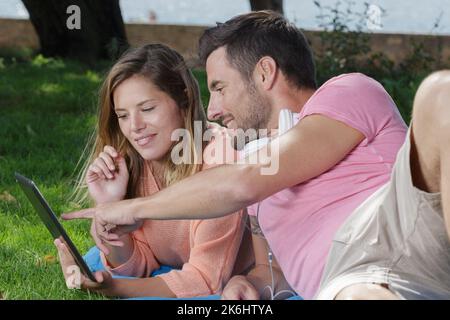 young beautiful happy couple using digital tablet in park Stock Photo
