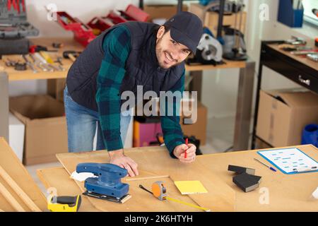 smiling joiner leaning over his workbench making notes Stock Photo