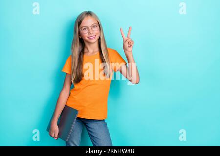 Photo of smart cute little girl wear orange t-shirt toothy smile hold laptop v-sign toothy smile enjoy home education isolated on aquamarine color Stock Photo