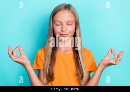 Photo of pretty cute girl wear orange stylish two arm demonstrate yoga symbol eyes closed relax rest isolated on cyan color background Stock Photo