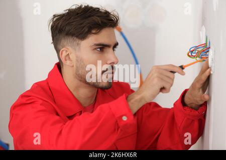 young male electrician using screwdriver on plug socket Stock Photo