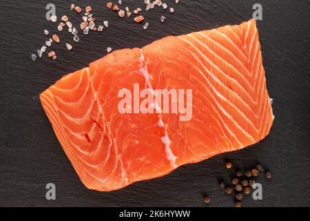 One piece of fresh salmon fillet with salt on slate stone, macro, top view. Stock Photo