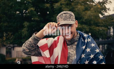 Cheerful soldier with american flag adjusting cap while smiling outside,stock image Stock Photo