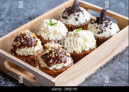 Cupcakes and muffins placed in wooden box. Chocolate and creme with nuts. Fresh home make baked sweets. Stock Photo