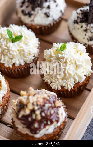 Cupcakes and muffins placed in wooden box. Chocolate and creme with nuts. Fresh home make baked sweets. Stock Photo