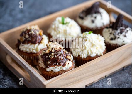 Cupcakes and muffins placed in wooden box. Chocolate and creme with nuts. Fresh home make baked sweets. Stock Photo