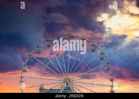 Ferris Wheel and illuminations in amusement park during scenic sunset with dramatic sky clouds and flying birds Stock Photo