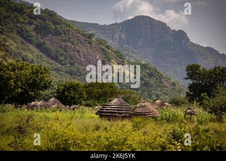 Beautiful grass thatch mud houses lay in a valley below the hills and mountains of Abim District, Uganda, East Africa. Stock Photo