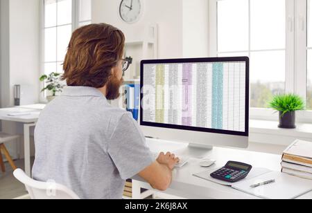 Busy financial accountant sitting at office desk and working with spreadsheets on computer Stock Photo