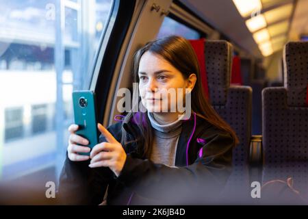 Interested female traveler filming landscapes behind glass in express train Stock Photo