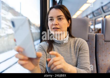 Woman taking photos with smartphone through window glass while travelling by train Stock Photo