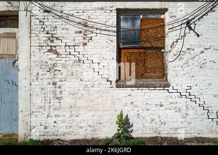 Boarded window and electrical wires on an abandoned white brick building Stock Photo
