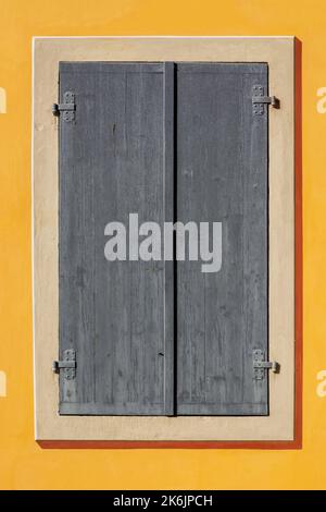 Rectangular window is covered with gray wooden shutters against a yellow wall. From the Window of the World series. Stock Photo