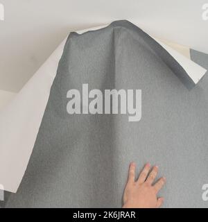 A man glues vinyl wallpaper on the wall, repair in the room and wallpapering, gray wallpaper. Stock Photo