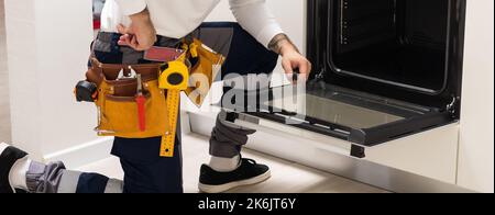 Professional serviceman repairing modern oven in kitchen Stock Photo