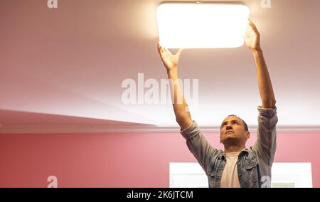 An electrician installs a chandelier on the ceiling. Hands of an electrician installing and connecting a lamp to a ceiling. Stock Photo