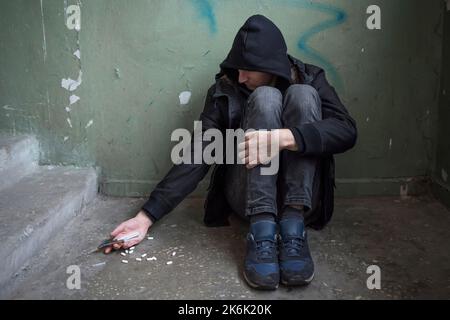 A male drug addict with a syringe is using drugs sitting on the floor. International Day Against Drug Abuse. Addiction concept. Stock Photo