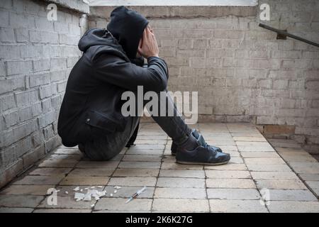 A young drug addict experiencing a drug addiction crisis, sitting in an abandoned house. Addiction concept. Lifestyle. Stock Photo