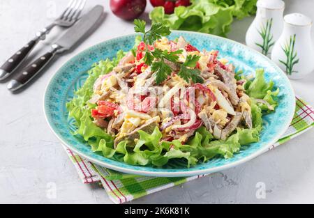 Salad with tongue, sweet peppers, eggs, cheese and lettuce leaves on blue plate on gray background, Close up Stock Photo