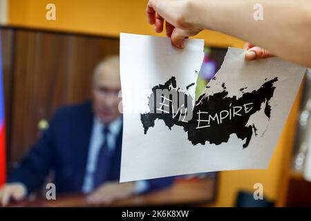 Hands tearing apart paper with black contours of Russia with a phrase Evil Empire written on it, in front of a tv set.Russia disintegration concept Stock Photo