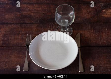 An empty white plate with a silver knife and fork and an empty glass. Stock Photo