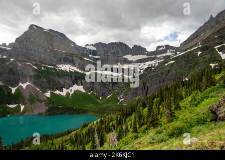 Photograph of the the Garden Wall, the shrinking Grinnell Glacier and Grinnell Lake from the Grinnell Glacier Trail on an overcast day. Glacier Nation Stock Photo