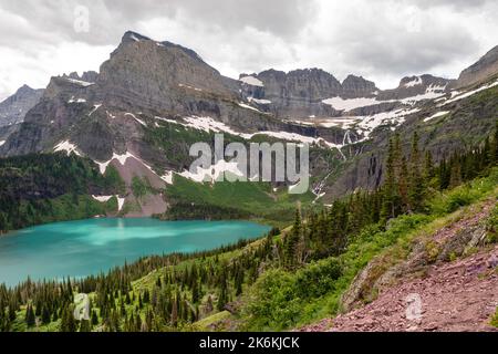 Photograph of the the Garden Wall, the shrinking Grinnell Glacier and Grinnell Lake from the Grinnell Glacier Trail on an overcast day. Glacier Nation Stock Photo