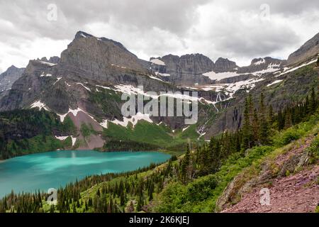 Photograph of the the Garden Wall, the shrinking Grinnell Glacier and Grinnell Lake from the Grinnell Glacier Trail on an overcast day. Glacier Nation Stock Photo