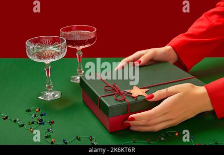 Womans hands with trendy red manicure holding gift box on green background Stock Photo