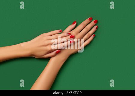 Womans hands with trendy christmas red manicure on green background Stock Photo