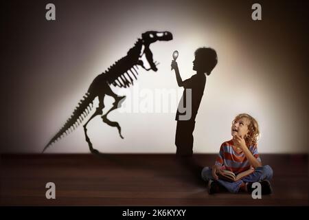 Dinosaur shadow in child dream. Kids read book and imagine future. Little boy dreaming to become a paleontologist. Children reading. Stock Photo