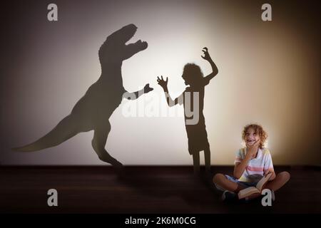 Dinosaur shadow in child dream. Kids read book and imagine future. Little boy dreaming to become a paleontologist. Children reading. Stock Photo