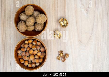 Hazelnuts and walnuts in a bowl with a few cracked next to it on the table. Flat lay. Stock Photo