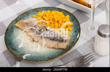 Sliced pickled herring fillet with corn and onions on plate Stock Photo
