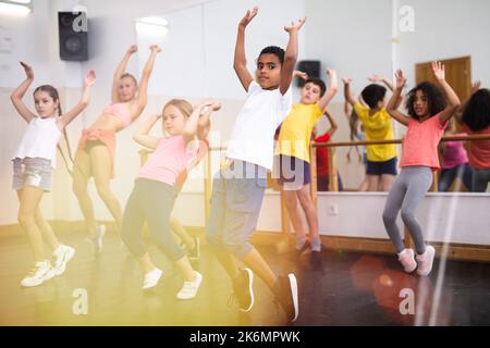 Preteen children practicing dance moves near ballet barre Stock Photo