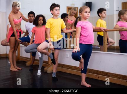 Preteen children practicing dance moves near ballet barre Stock Photo