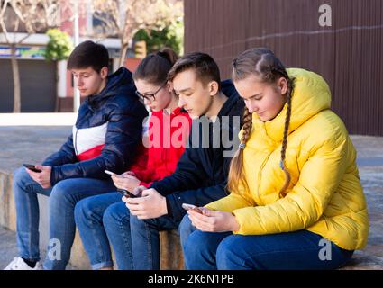Teenagers absorbed in phones outdoors Stock Photo