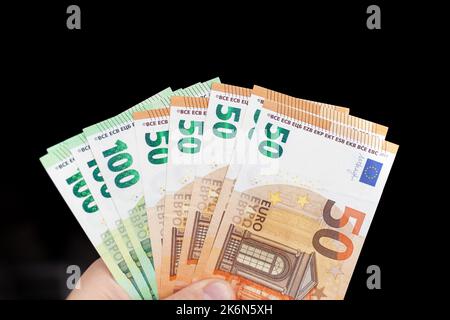 A man holds 100 euro banknotes in his hand on a dark background. cash paper currency, payment, earning and savings, money and finance concept. Empty s Stock Photo