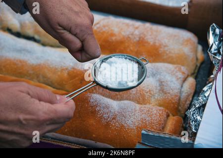 Baker pouring sugar over pastry on a bakery tray Stock Photo