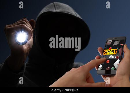 man in hood with smartphone and sport bet, hacker Stock Photo