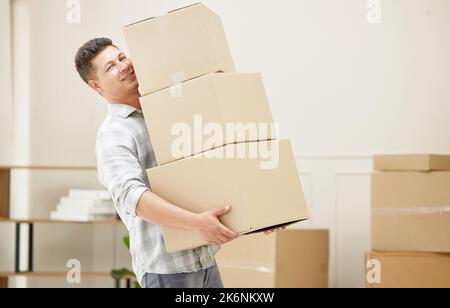 Never been this happy to move boxes. a handsome young man carrying boxes into his new home. Stock Photo