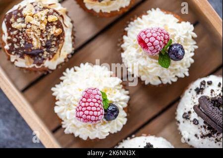 Tasty sweet muffins with mascarpone creme and chocolate, raspberry and blueberry. Fresh home baked sweets with fruit. Placed in wooden box. Stock Photo