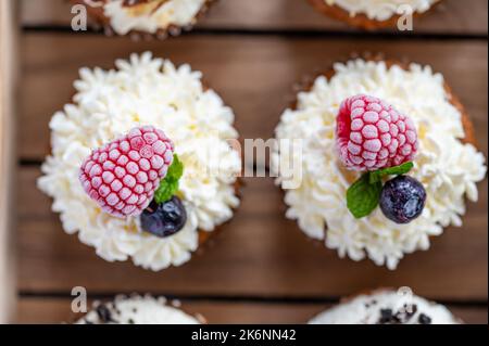 Tasty sweet muffins with mascarpone creme and chocolate, raspberry and blueberry. Fresh home baked sweets with fruit. Placed in wooden box. Stock Photo