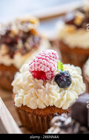 Tasty sweet muffins with mascarpone creme and chocolate, raspberry and blueberry. Fresh home baked sweets with fruit. Placed in wooden box. Stock Photo