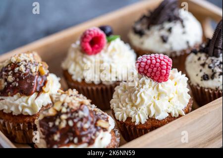 Tasty sweet muffins with mascarpone creme and chocolate, raspberry and blueberry. Fresh home baked sweets with fruit. Placed in wooden box. Stock Photo