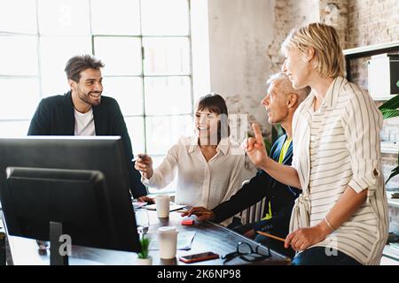Creative business team sharing laptop in office, watching startup presentation, design project, discussing ideas, brainstorming, pointing at monitor, Stock Photo