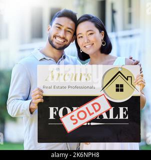 Portrait of a smiling young couple by sold sign standing against sky ...