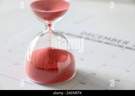 Red sand running through bulbs of hourglass, on December calendar, measuring passage of time, end of year, time running out concept Stock Photo