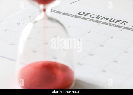 Running out of time concept, December calendar, hourglass running out of time in the foreground but out of focus, countdown to end of year Stock Photo